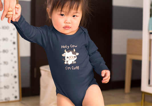 A cute and super soft baby onesie featuring a baby cow image in the middle with the words 'holy cow I'm cute' in light beige lettering around the image.