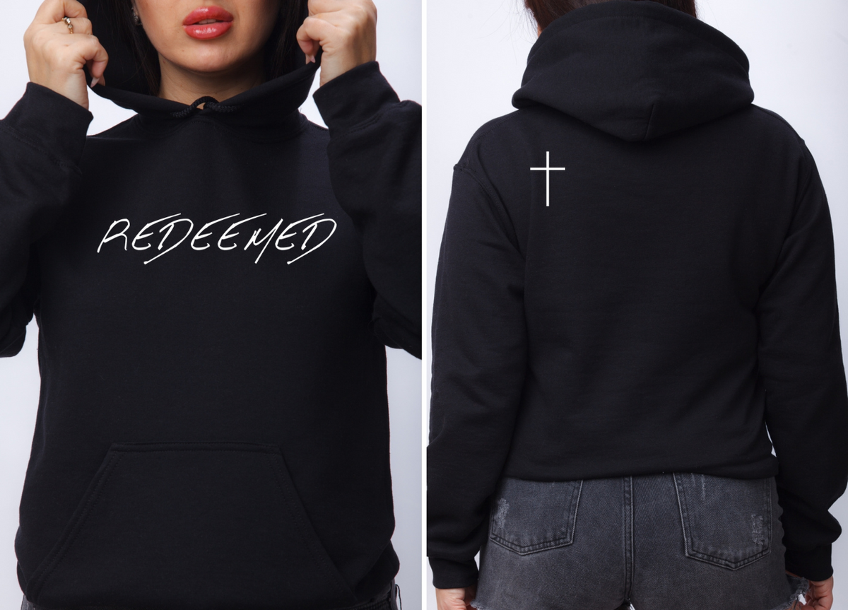 A black hoodie with the words redeemed on the front center, a Jesus cross is on the back left shoulder of the hoodie.