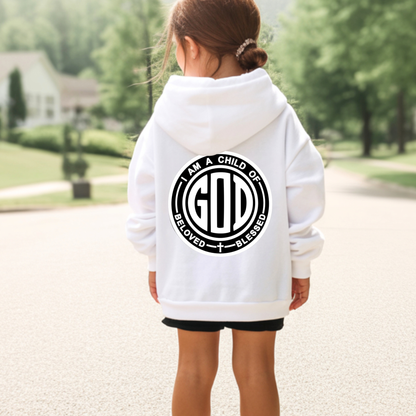 A child viewed from behind wearing a white pullover hoodie with a large black circular graphic on the back that reads 'I AM A CHILD OF GOD' and 'BLESSED / BLESSED.' The child is standing outdoors on a paved path with trees and a house blurred in the background.