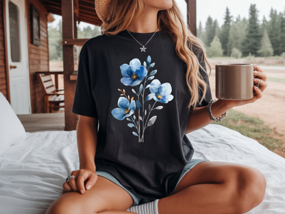 A woman wearing a black short-sleeve t-shirt with a blue and white floral graphic on the front, styled with a white collared shirt underneath and a brown hat.