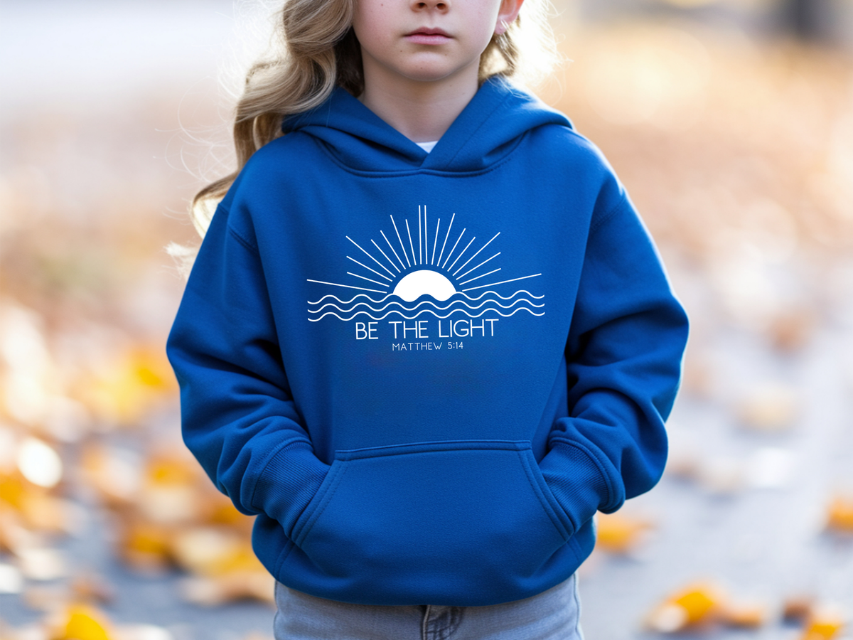 A blue youth hoodie with an image of the sun and waves underneath with the words Be the Light Matthew 5:14 
