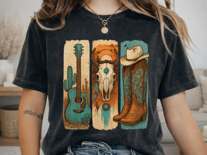 A woman wearing a grey graphic t-shirt with a western-themed print featuring a turquoise guitar, a brown skull, and a cowboy boot. The background shows a room with a wooden door, a hat on a shelf, and a striped shirt hanging on a rack.