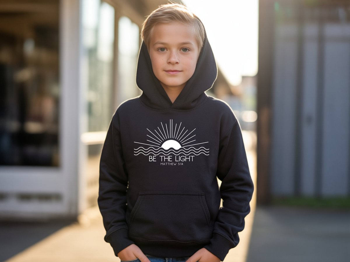 A black youth hoodie with an image of the sun and waves underneath with the words Be the Light Matthew 5:14 