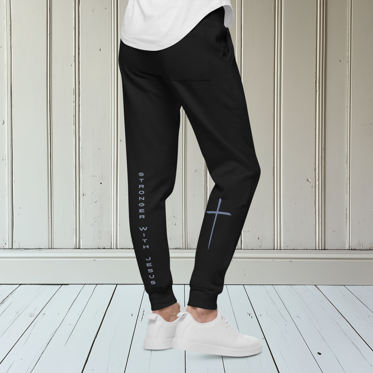 A pair of fleece lined sweatpants that have the words Stronger With Jesus on the back left leg of the pants, on the right leg is a large Jesus cross