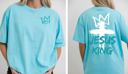 A oversized graphic t-shirt with an image of a crown spray painted on the top right chest of the shirt, on the back of the shirt is a large cross spray painted on the back with a cross on the top with the words 'Jesus is King' spray painted on the top.
