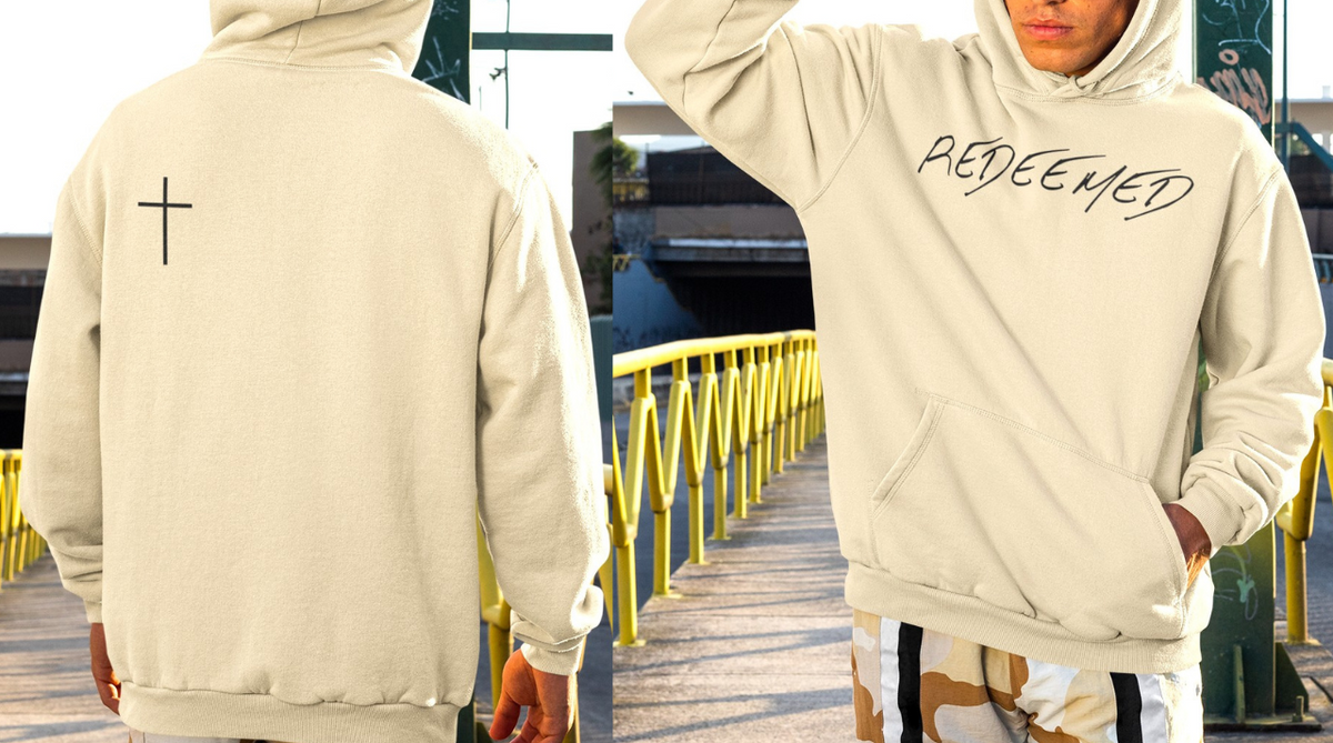 A beige hoodie with the words redeemed on the front center, a Jesus cross is on the back left shoulder of the hoodie.