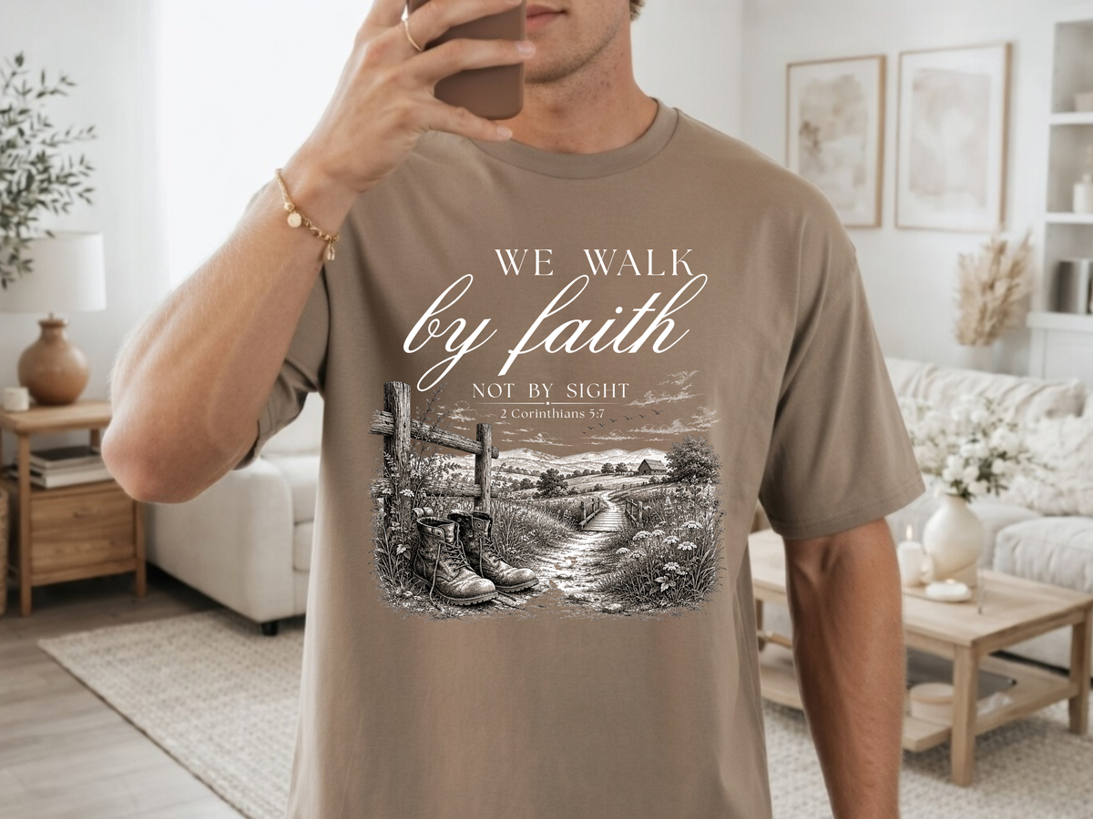 A Christian t-shirt with an image of a path cutting through fields and trees with a barn in the background and a fence with a pair of boots sitting in front, the words We walk by faith not by sight 2 Corinthians 5:7 are just above the image.