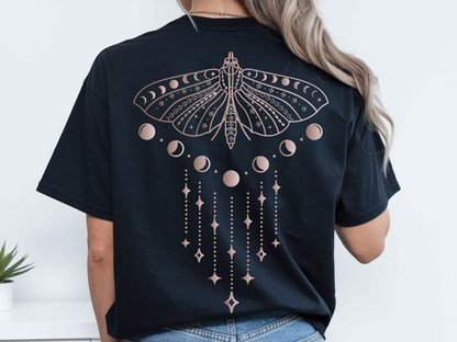 A woman modeling an oversized black washed T-shirt shown from both front and back. The front is plain, while the back features a large pale pink moon-phase dragonfly graphic.