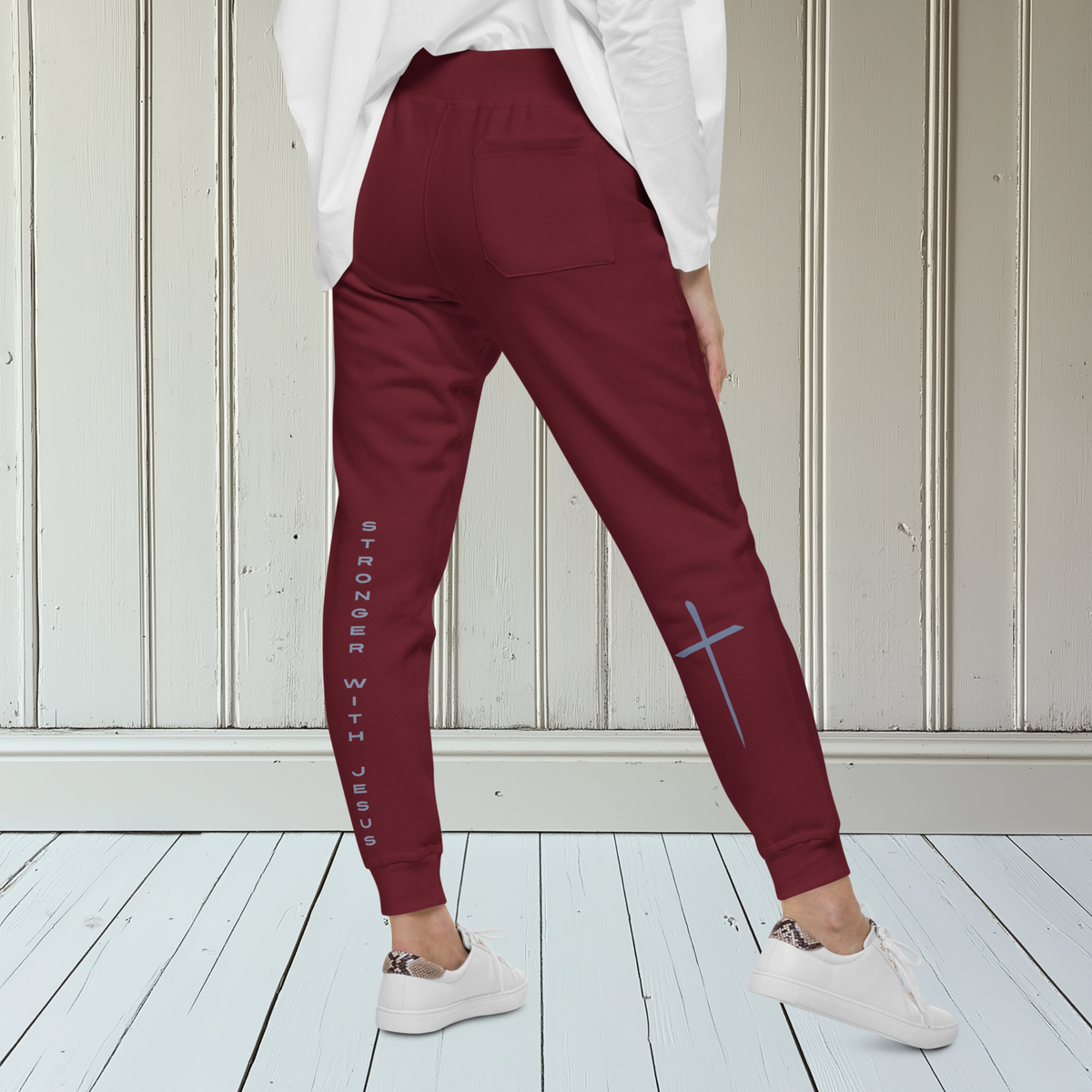 A pair of fleece lined sweatpants that have the words Stronger With Jesus on the back left leg of the pants, on the right leg is a large Jesus cross