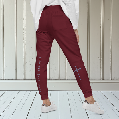 A pair of fleece lined sweatpants that have the words Stronger With Jesus on the back left leg of the pants, on the right leg is a large Jesus cross