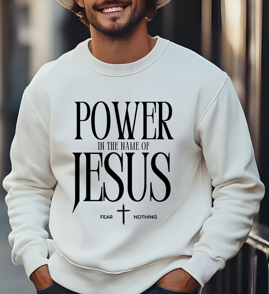 On the front of this Christian pullover sweatshirt it says Power In The Name Of Jesus with a Jesus cross underneath it, on either side of the cross are the words Fear and Nothing.