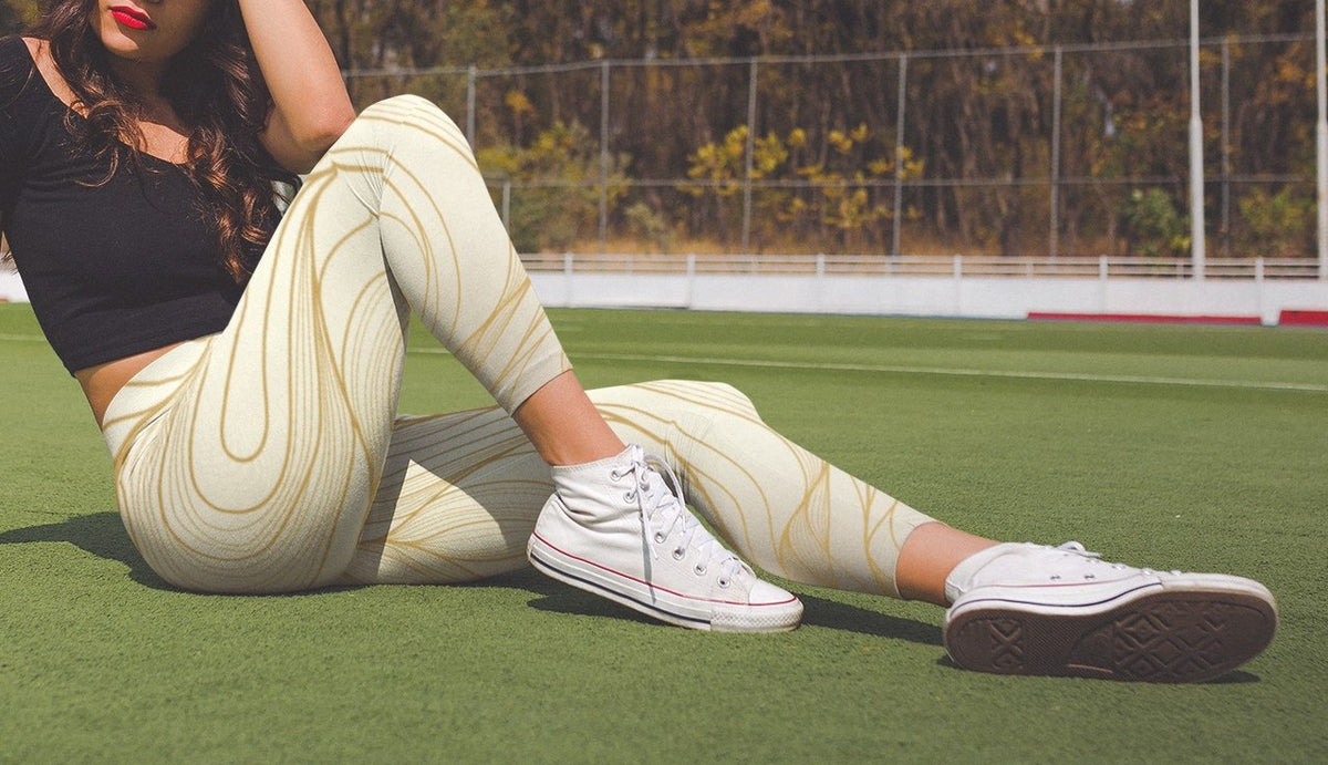 A pair of women's high waisted leggings, they are beige in color with abstract gold lines all over the pants.