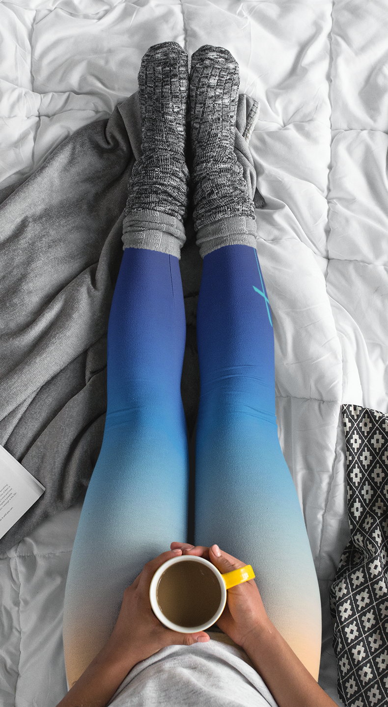 A pair of high waisted ombre leggings that start as a light orange then fade to a dark blue at the bottom, there is a light blue Jesus cross on the right ankle of the pants.