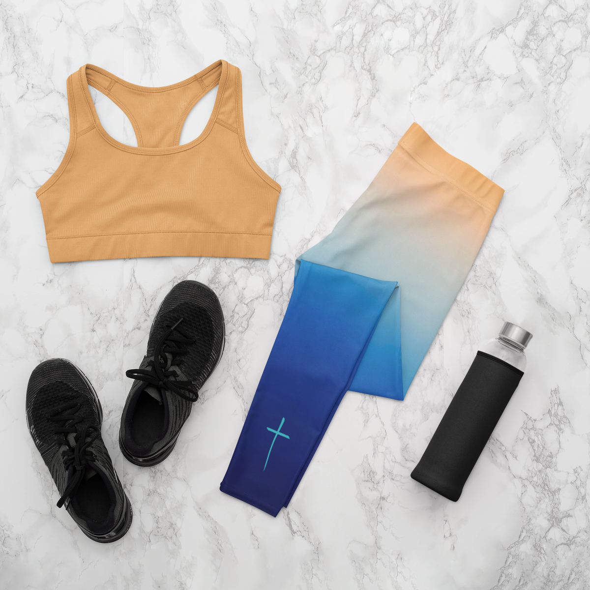 A pair of high waisted ombre leggings that start as a light orange then fade to a dark blue at the bottom, there is a light blue Jesus cross on the right ankle of the pants.