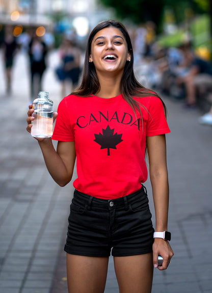 Woman wearing a red 'Canada' t-shirt with a maple leaf graphic on a city street.